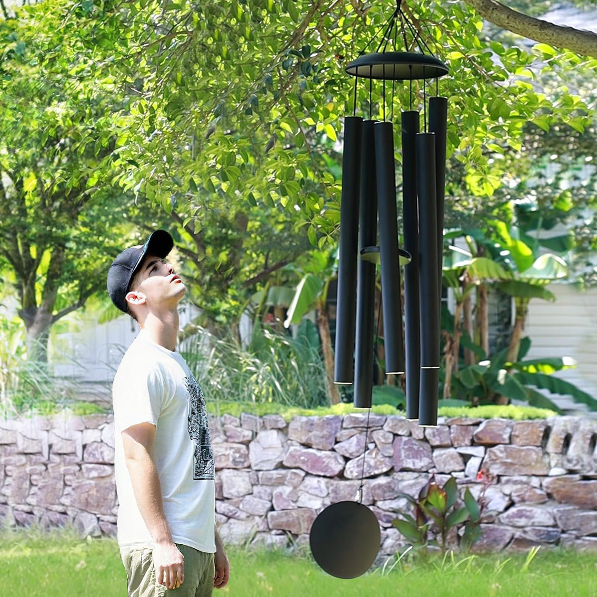 Outdoor scene of a man looking up at large black wind chimes hanging from a tree in a yard