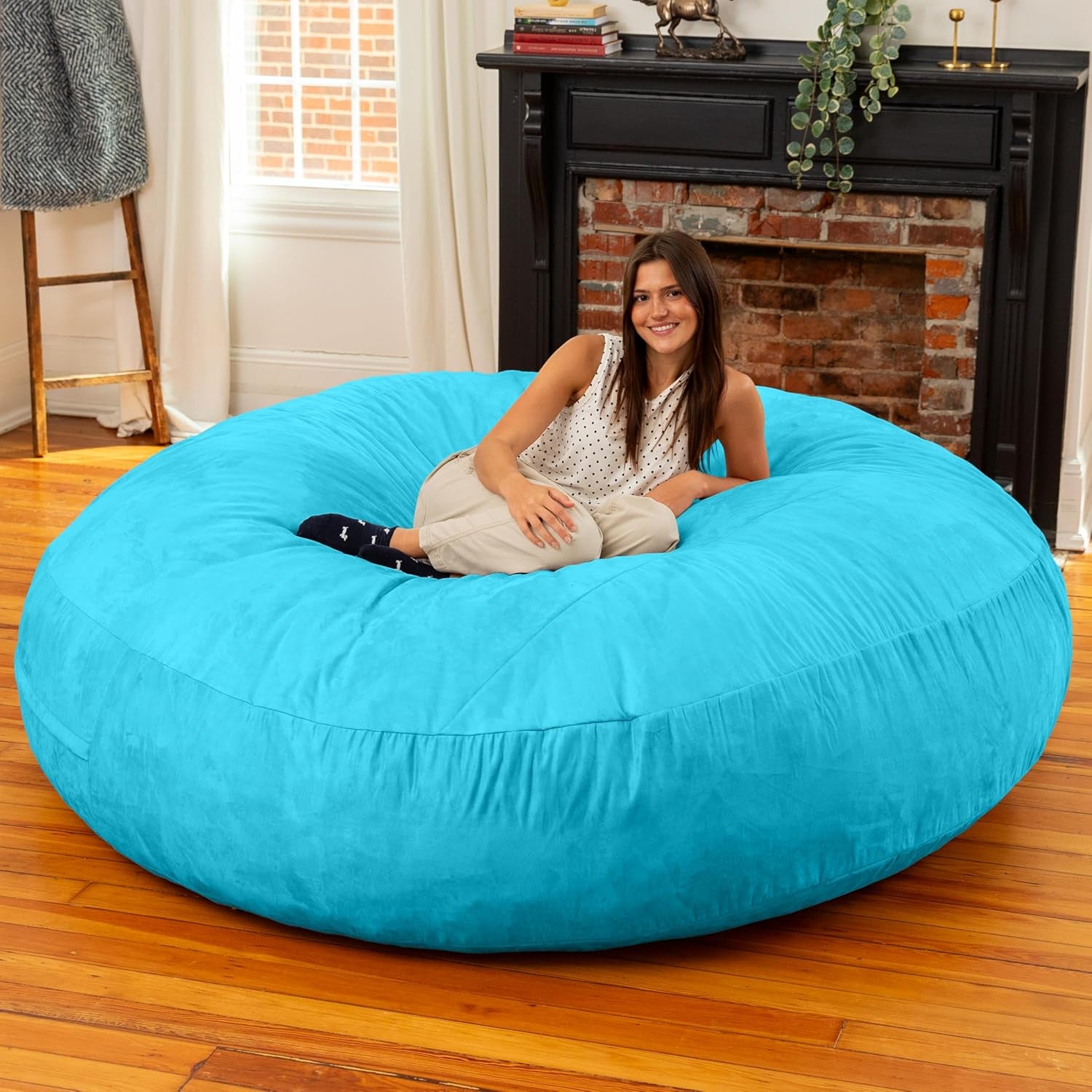 Woman sitting on a bright turquoise round bean bag in a sunlit room with a fireplace.