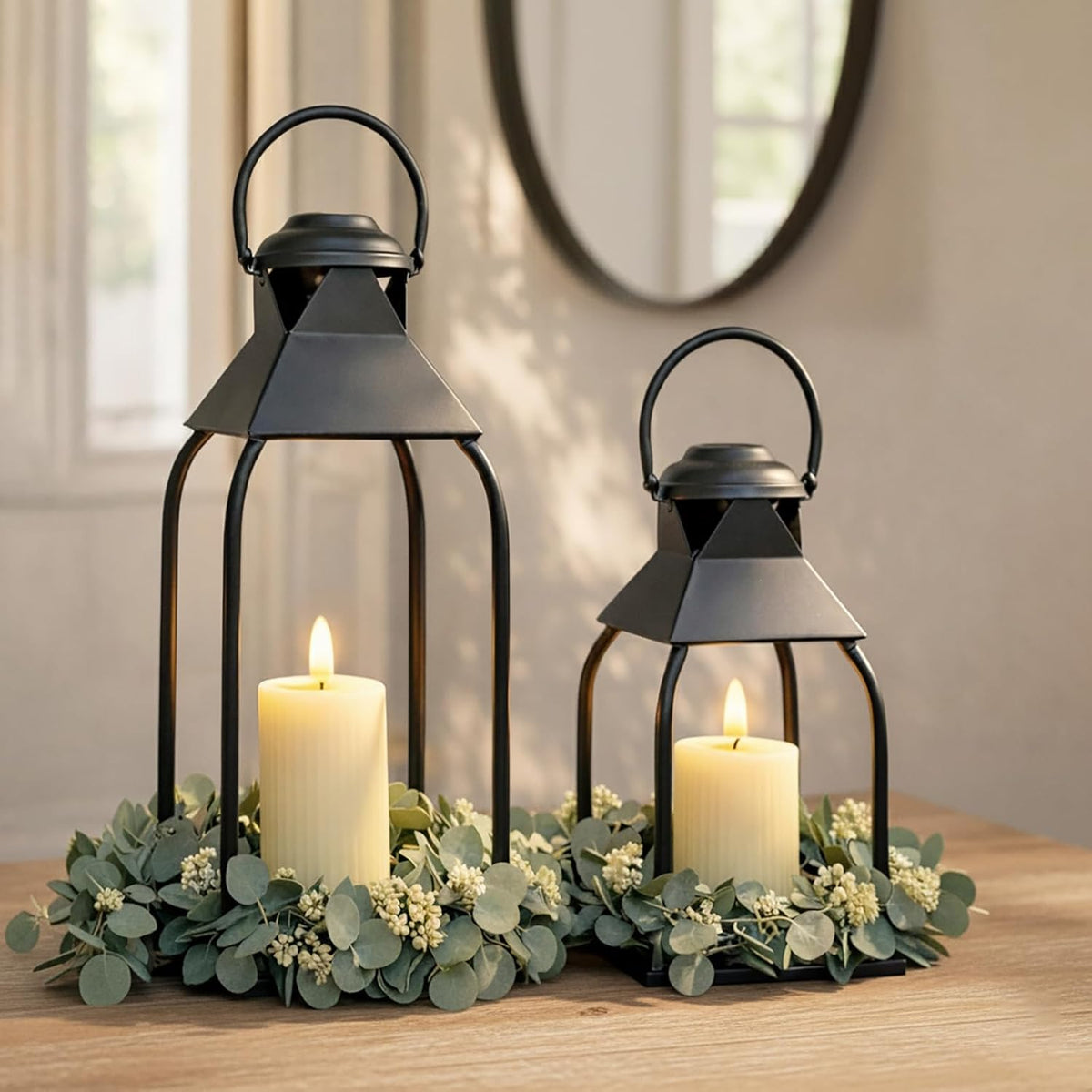 Close view of two black lanterns with glowing candles and a round wall mirror blurred in the background.