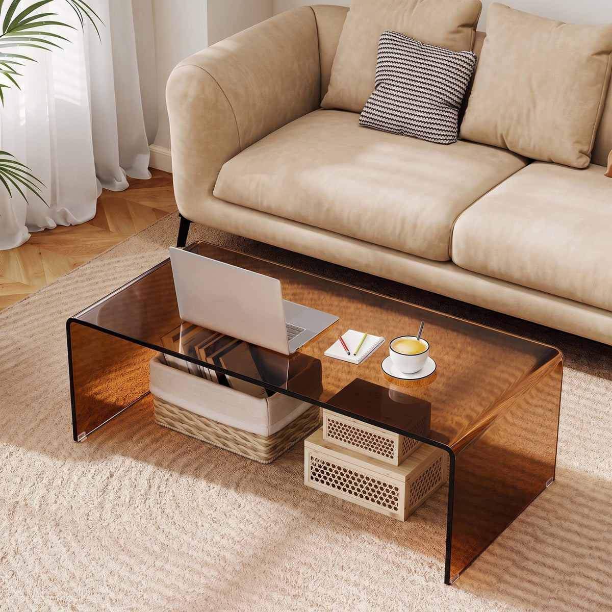 Glass coffee table beside a beige sofa, with a laptop, cup, and small storage baskets underneath.