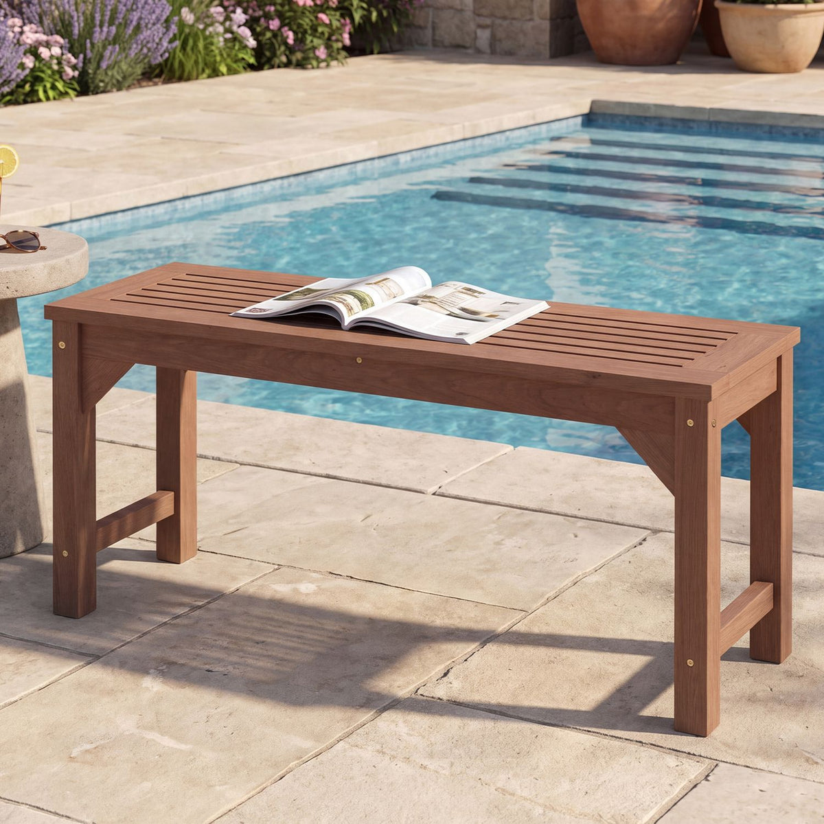 Brown slatted backless bench beside a swimming pool, with an open book resting on the seat.