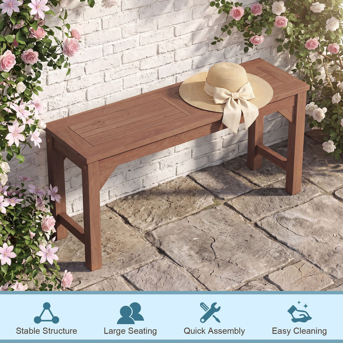 Brown slatted bench against a white brick wall, with a straw hat on the seat and flowers around it.