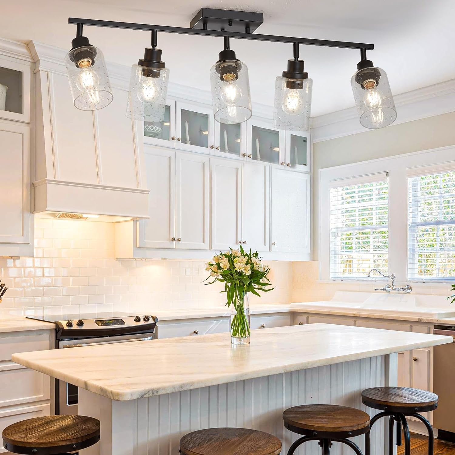 Five-light track fixture with seeded glass shades above an island, angled view in a bright kitchen