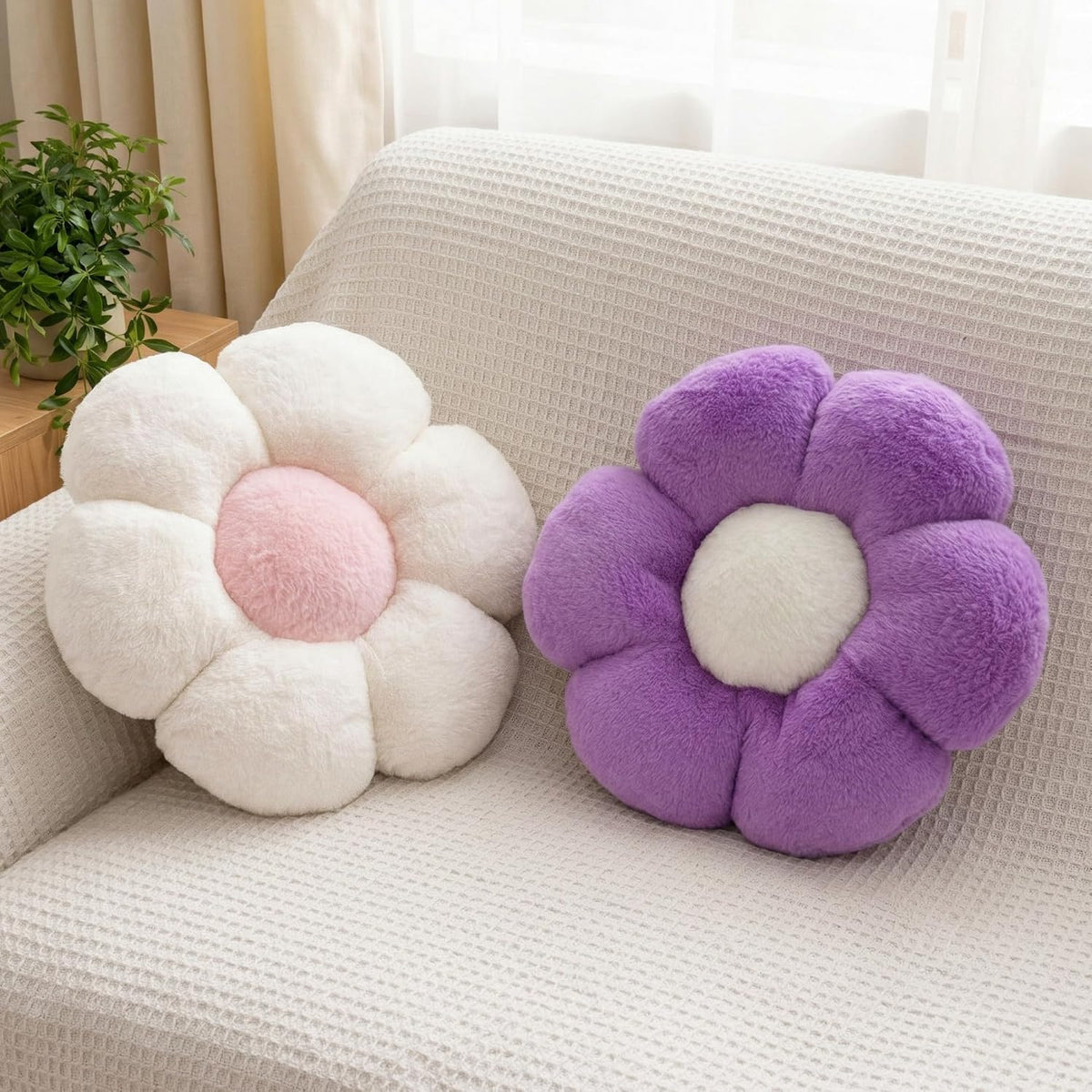 Two flower-shaped plush pillows — one cream with a pink center and one lavender with a white center — on a waffle-textured