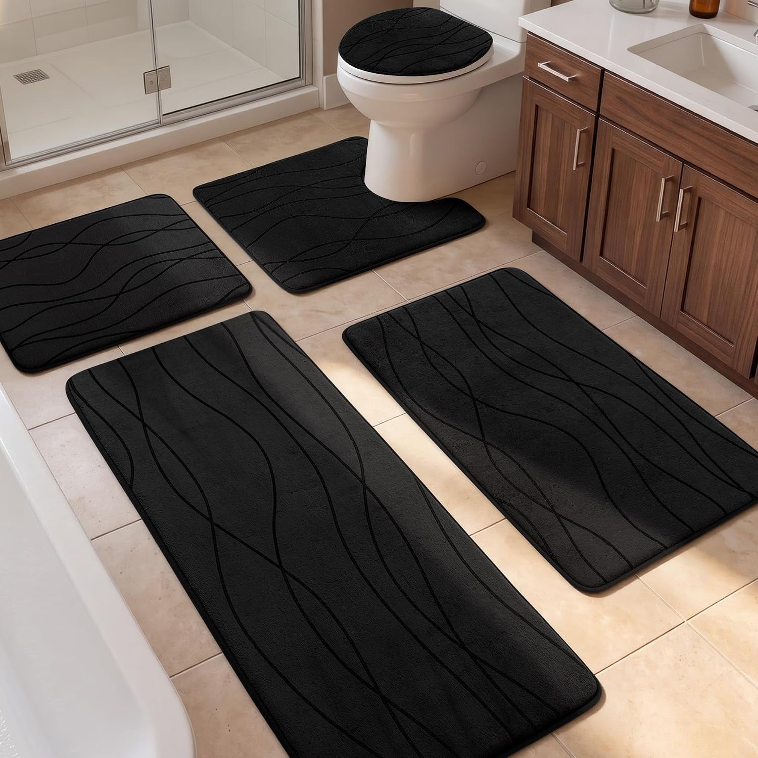 Four black bath rugs, including a toilet lid cover, arranged on beige tile in front of a vanity