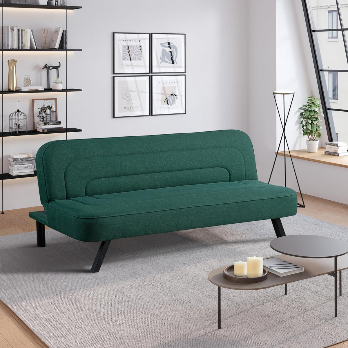 Green upholstered futon sofa with angled black metal legs in a bright living room setting.