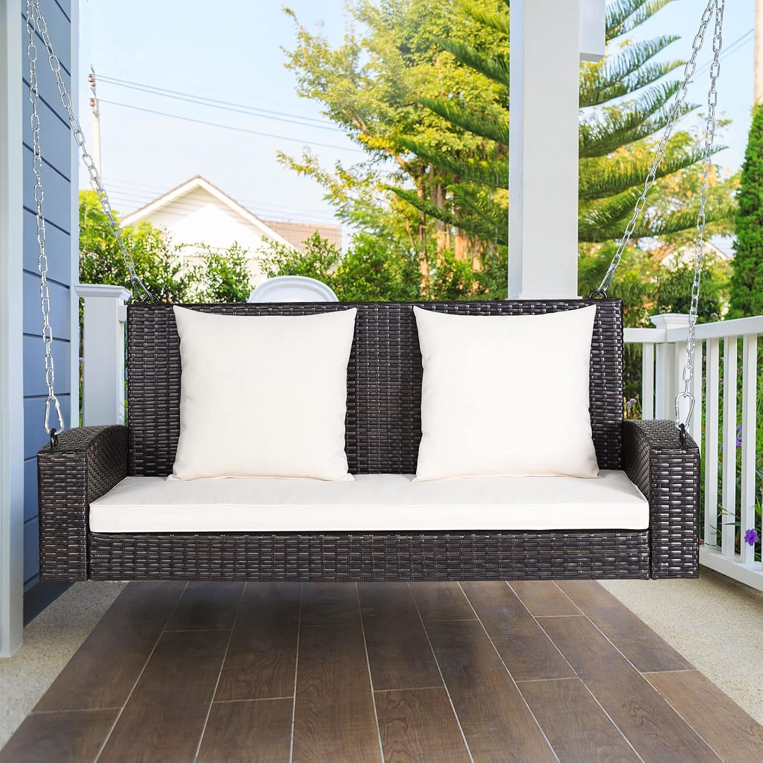 Front view of dark brown rattan 2-seat hanging porch swing with cream seat and back cushions on a covered porch