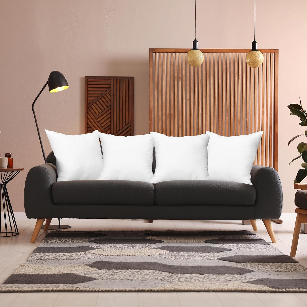Four white pillow inserts arranged on a dark grey sofa in a styled living room setting