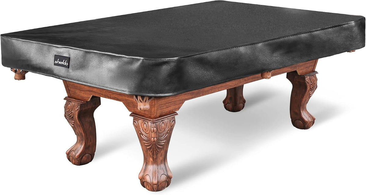 Three-quarter view of a wooden pool table fully covered by a fitted black leatherette cover