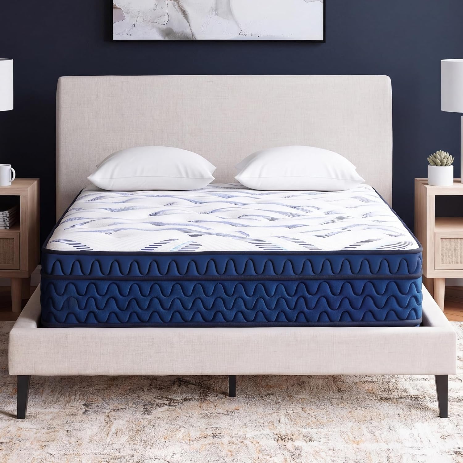 Front-facing bedroom shot of a navy blue hybrid mattress with white patterned top on a beige upholstered bed, two pillows