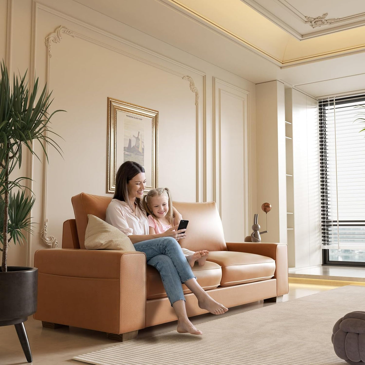 Angled scene of the brown faux leather loveseat with a woman and child seated in a bright living room setting.