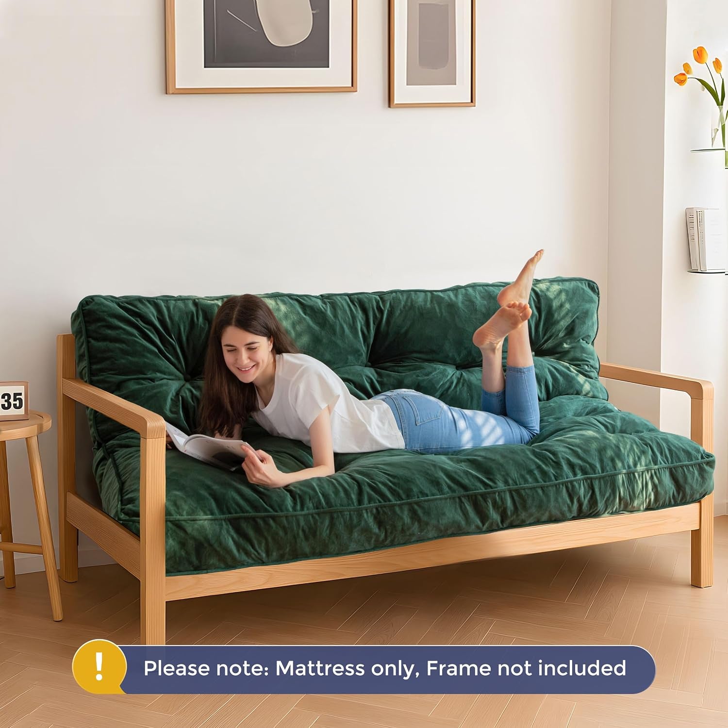 Person lying on a dark green tufted futon mattress on a wooden sofa frame in a bright room
