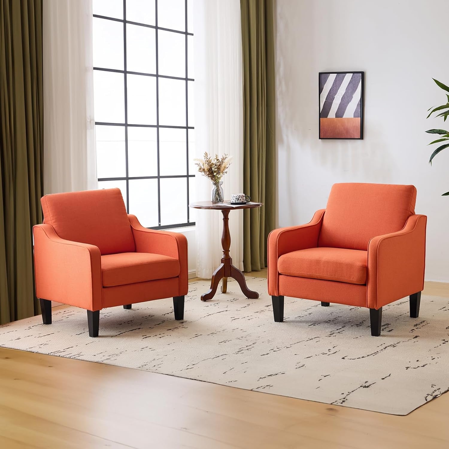 Two bright orange upholstered accent chairs flanking a small round wooden table in a sunlit room.