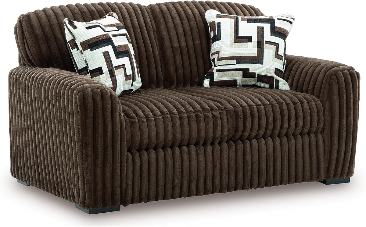 Plush oversized chocolate-brown corduroy lounge chair with two patterned throw pillows.
