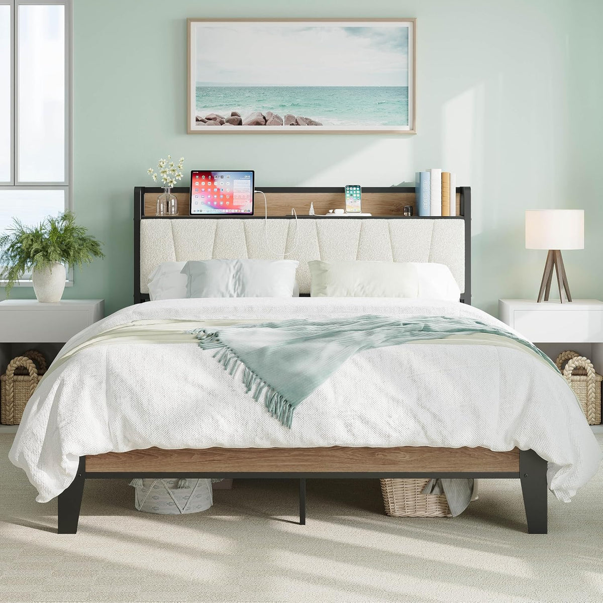 Front view of bed with pale wood shelf headboard holding a phone and tablet, white bedding and light green throw.
