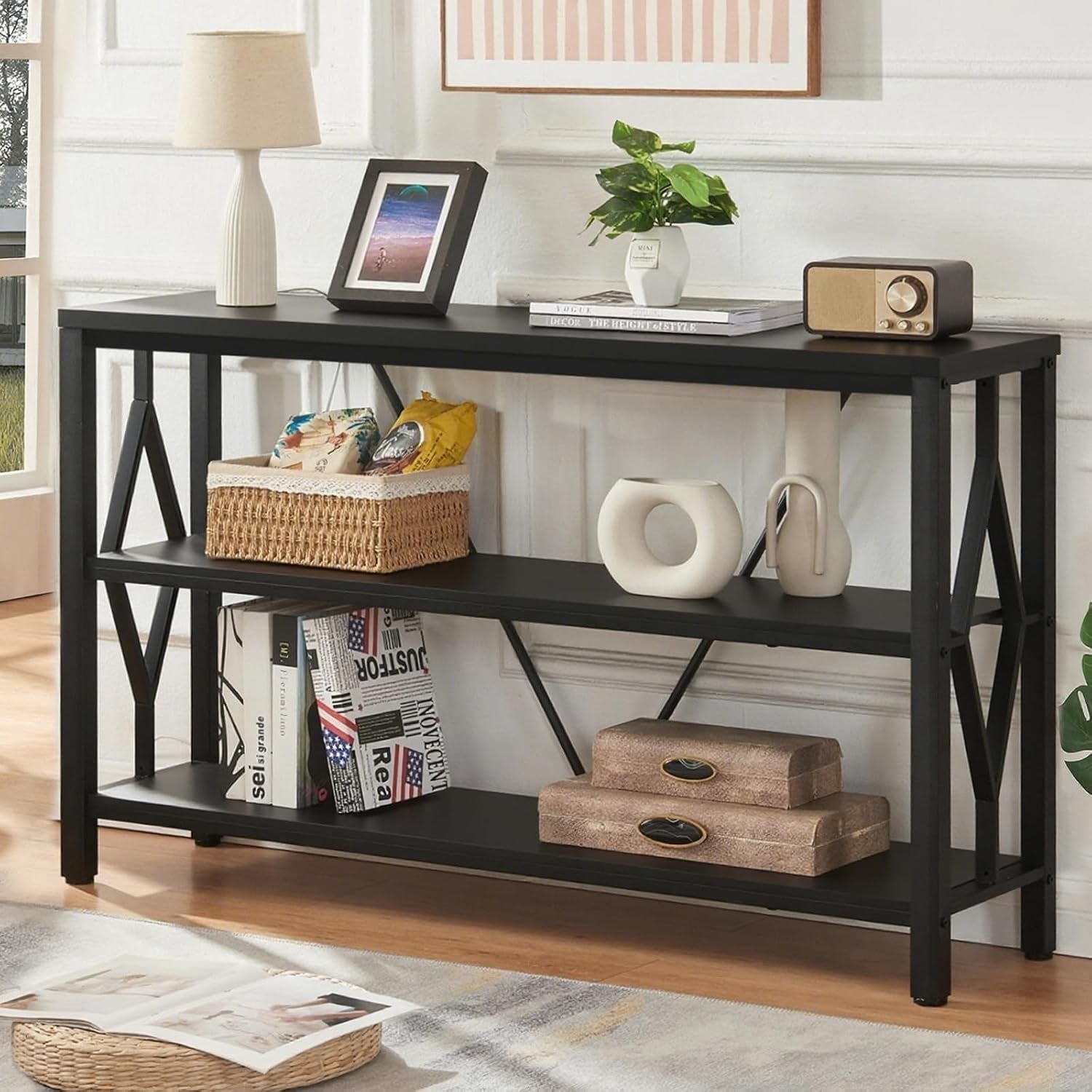 Black three-tier console table with diamond metal side supports against a white paneled wall, styled with decor.