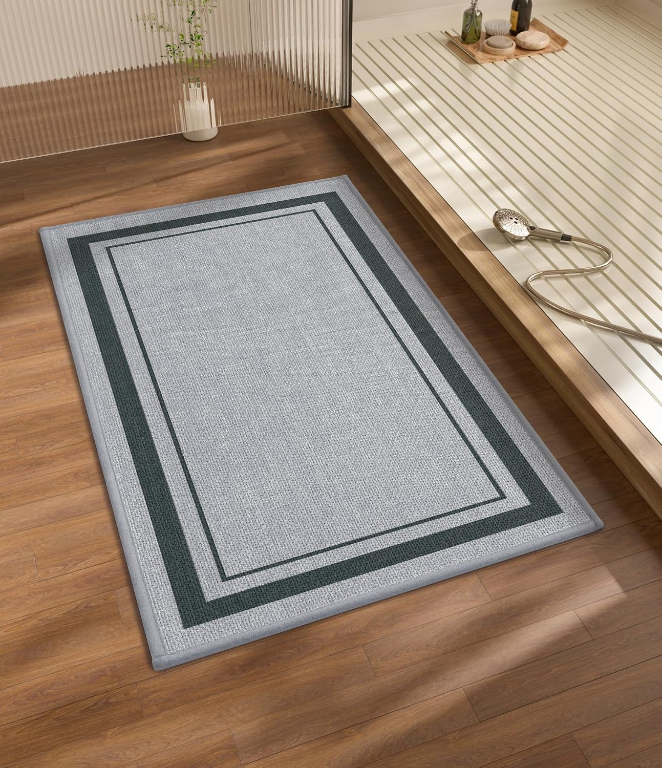 Light gray rectangular rug with dark greenish borders on wood floor near a shower tray
