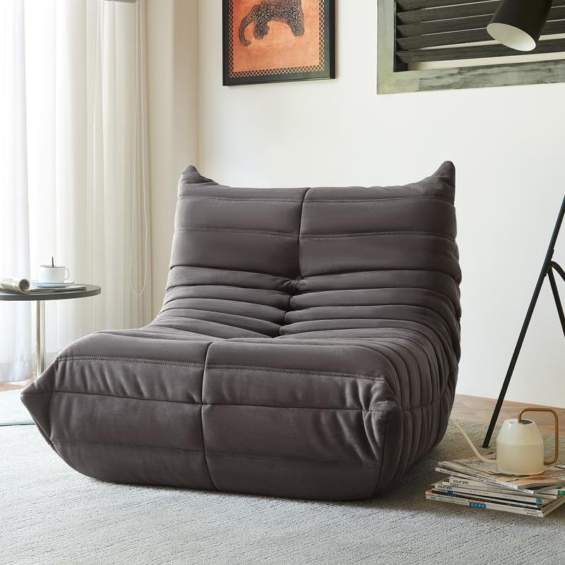 Charcoal single lounge chair angled front beside a floor lamp and stacked magazines.