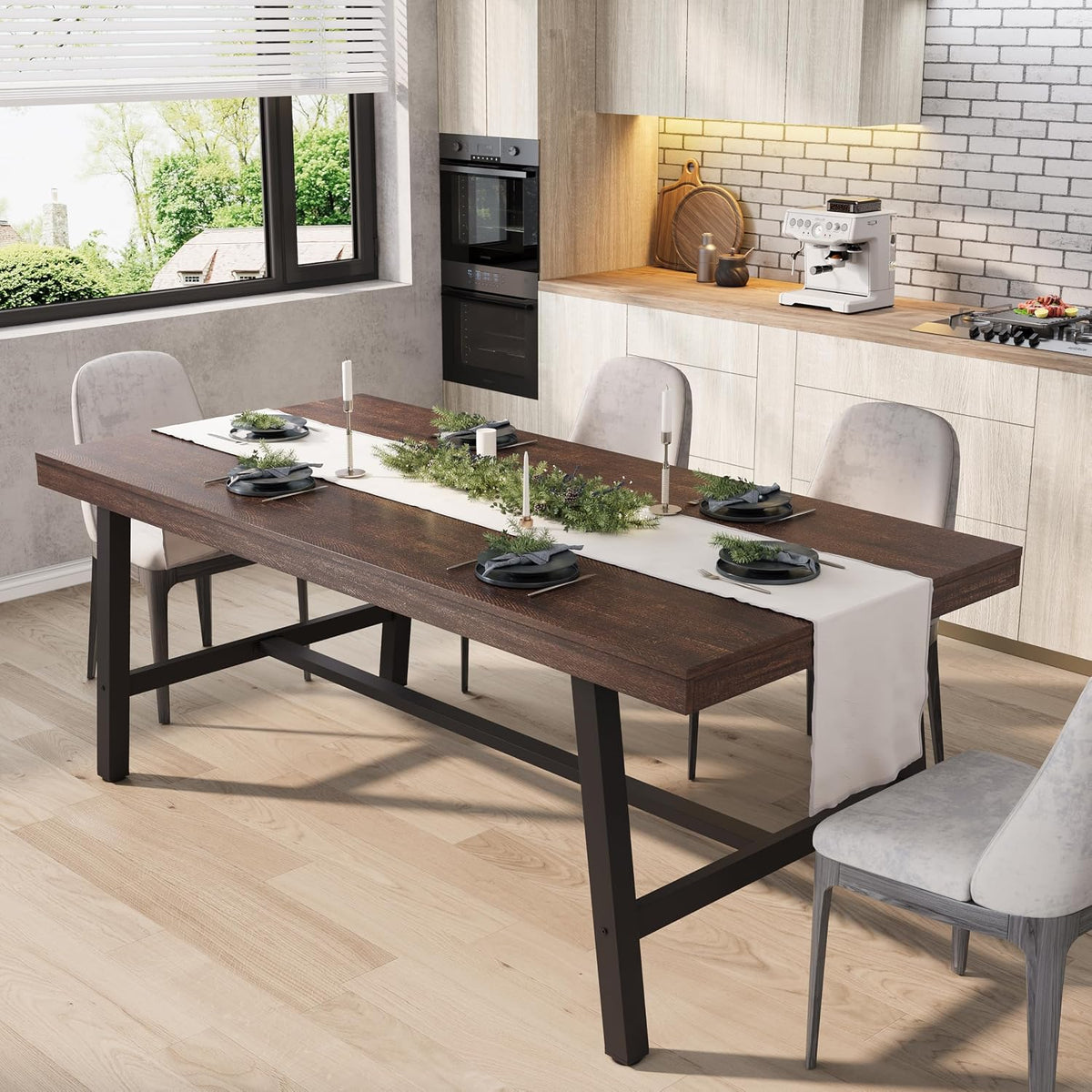 Dining table with dark brown wood top and black metal legs set with a white runner and candles in a bright kitchen.