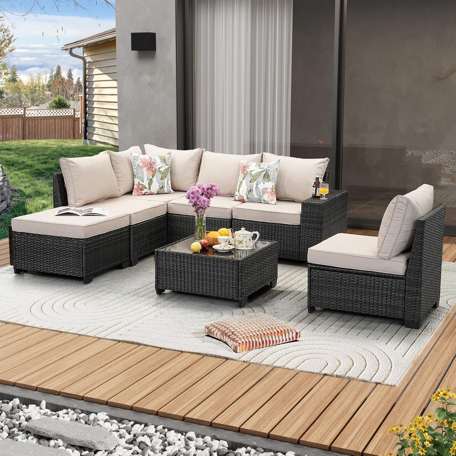 Beige-cushioned rattan sectional arranged in an L-shape with a matching glass-top coffee table on a deck.