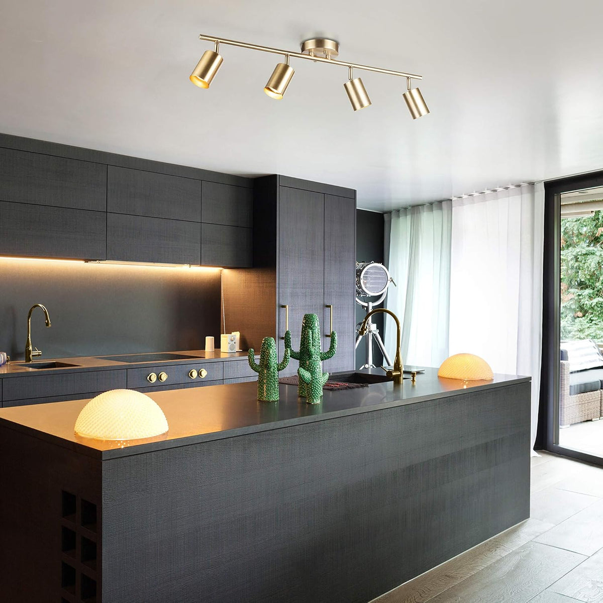 Matte brass 4-light track fixture mounted on a kitchen ceiling over a dark cabinetry island, angled perspective