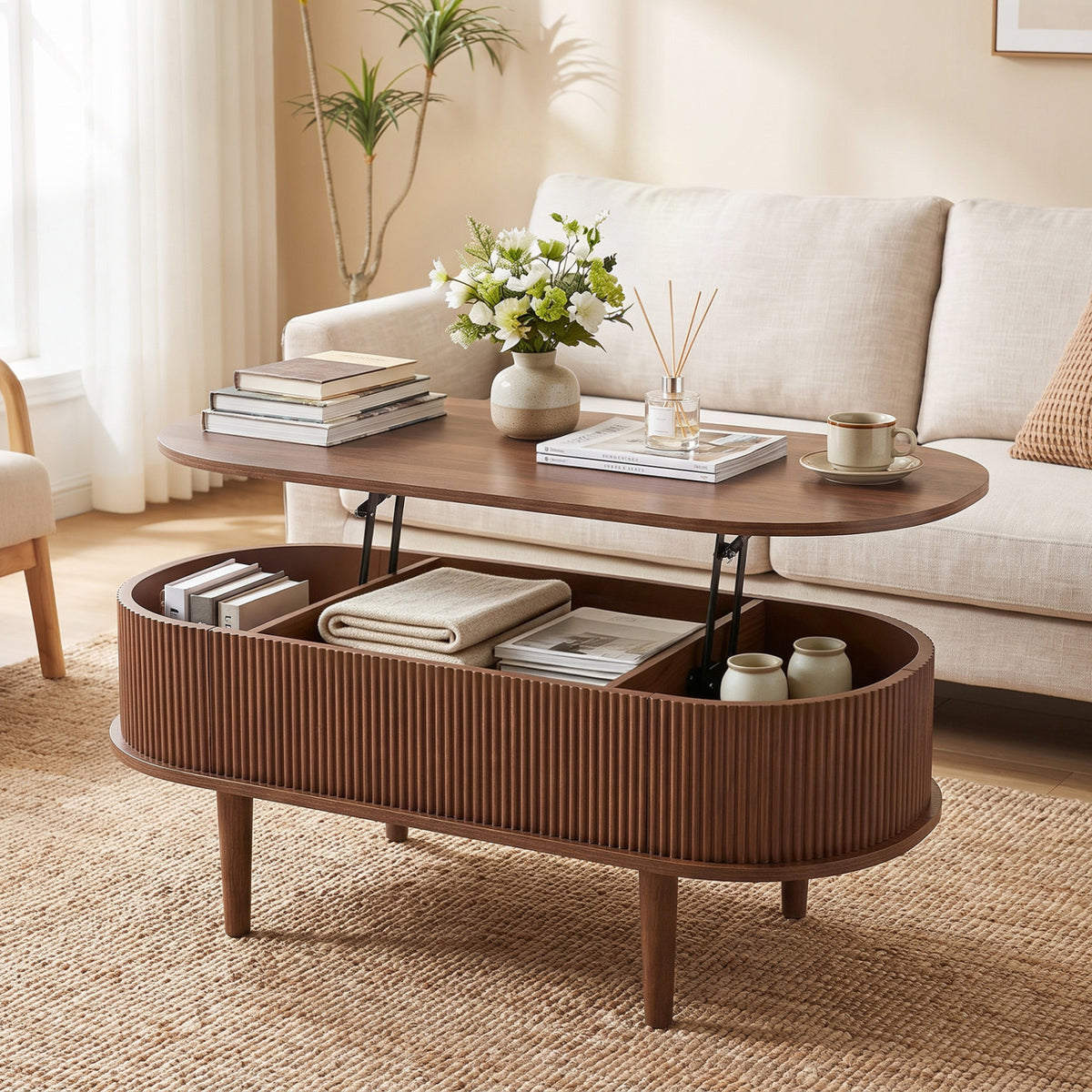 Oval fluted coffee table with its top raised, showing divided storage filled with books, a folded throw, and cups.