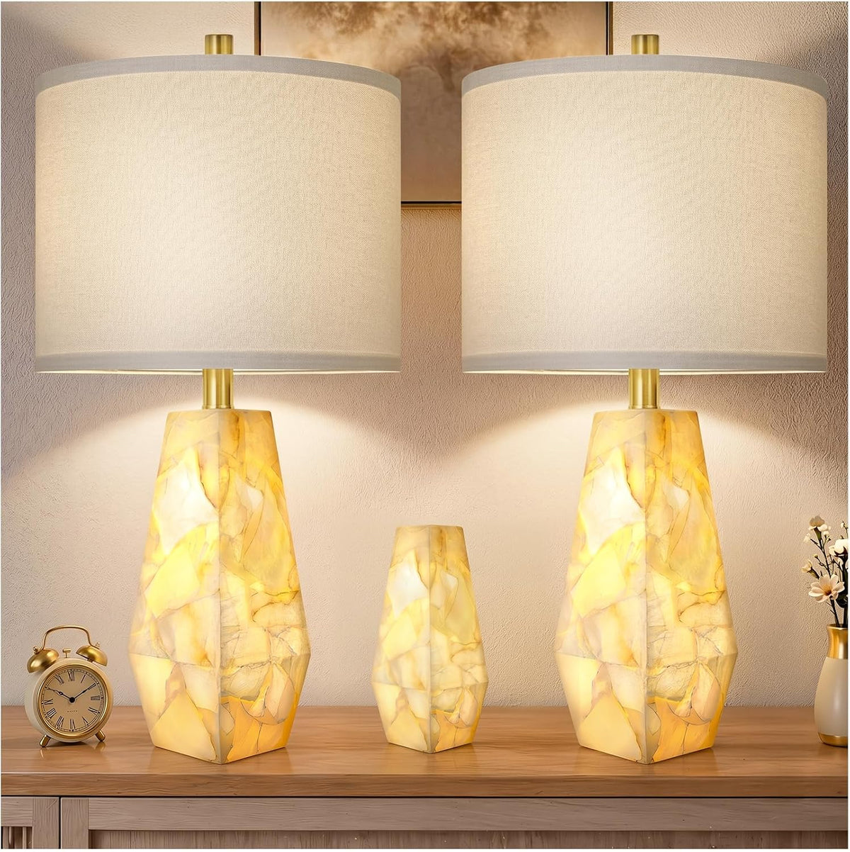Two faceted alabaster lamps flanking a small matching nightlight on a dresser with an alarm clock and a small vase.