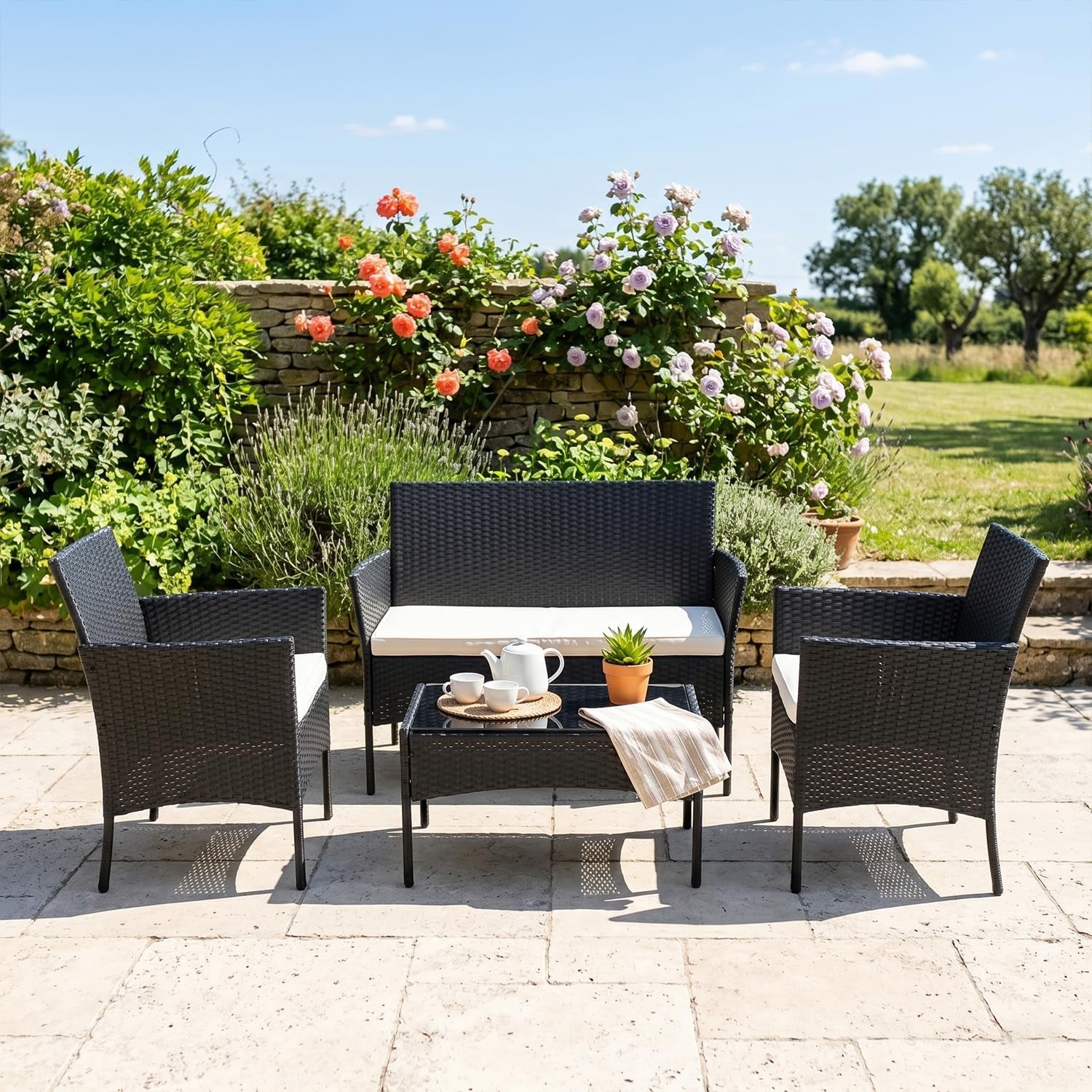 Outdoor garden scene with the same four-piece rattan seating set arranged on a stone patio with plants behind.