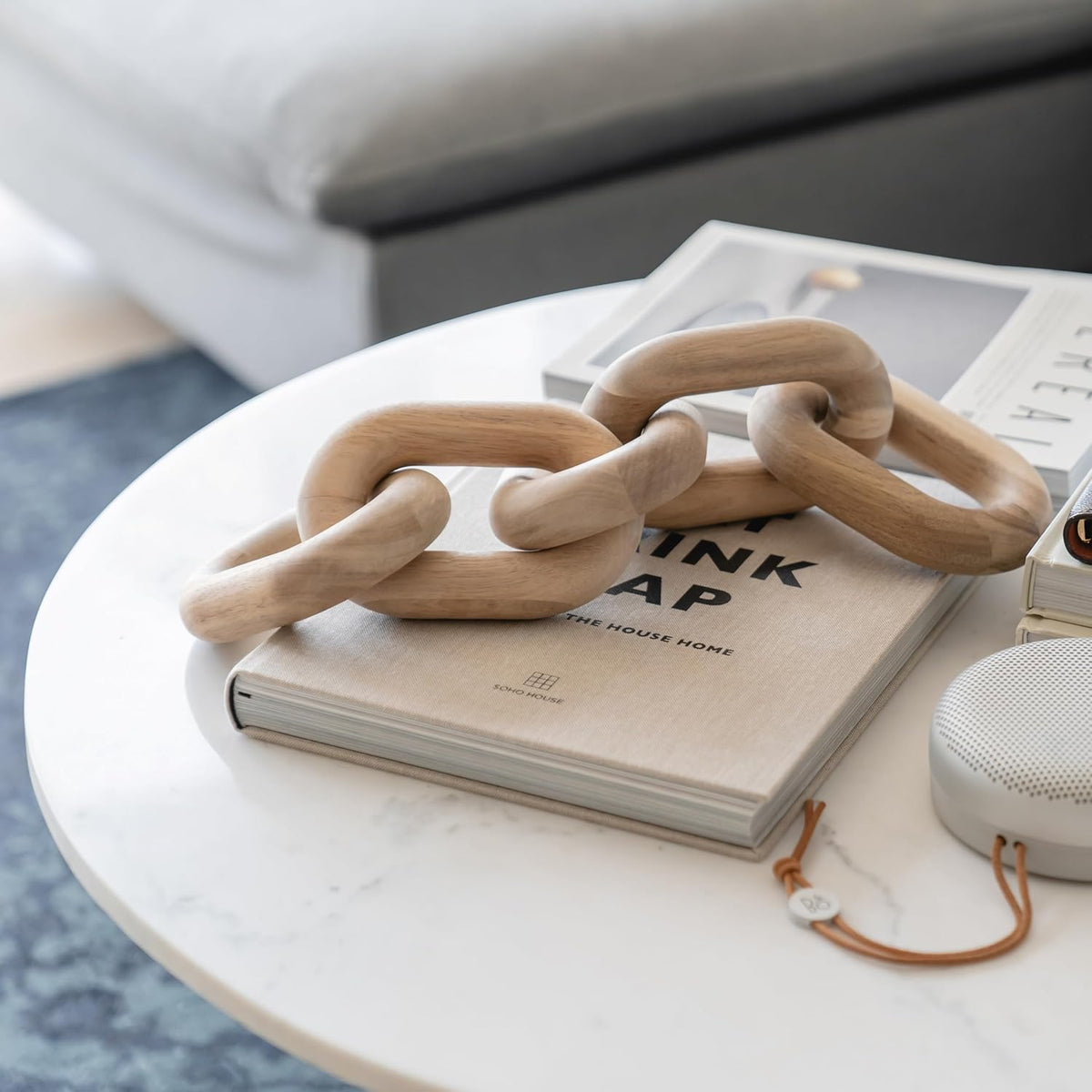 Acacia wood link chain draped over a neutral hardcover on a round white coffee table, angled side view.