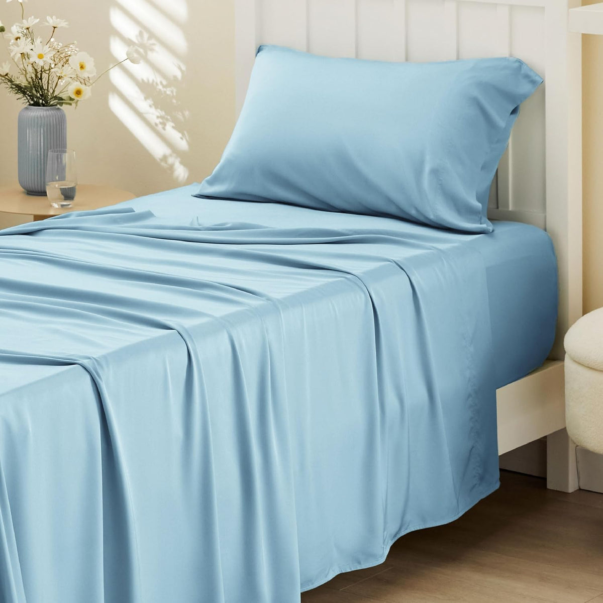 Light blue sheets and pillow on a single bed with a white slatted headboard and bedside table.