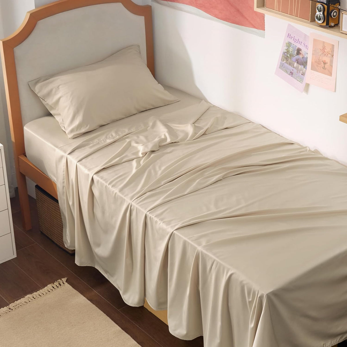 Single bed side view with beige silky sheet and pillow draped over the mattress and floor storage nearby