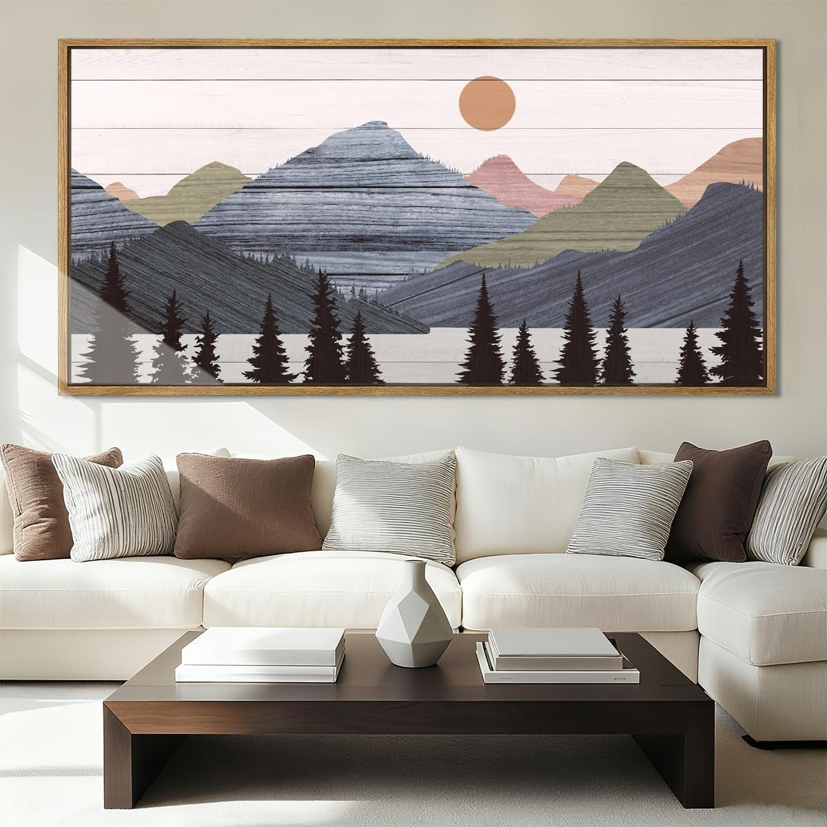 Wide framed landscape print of layered mountains and trees hung above a cream sectional sofa and wooden coffee table.