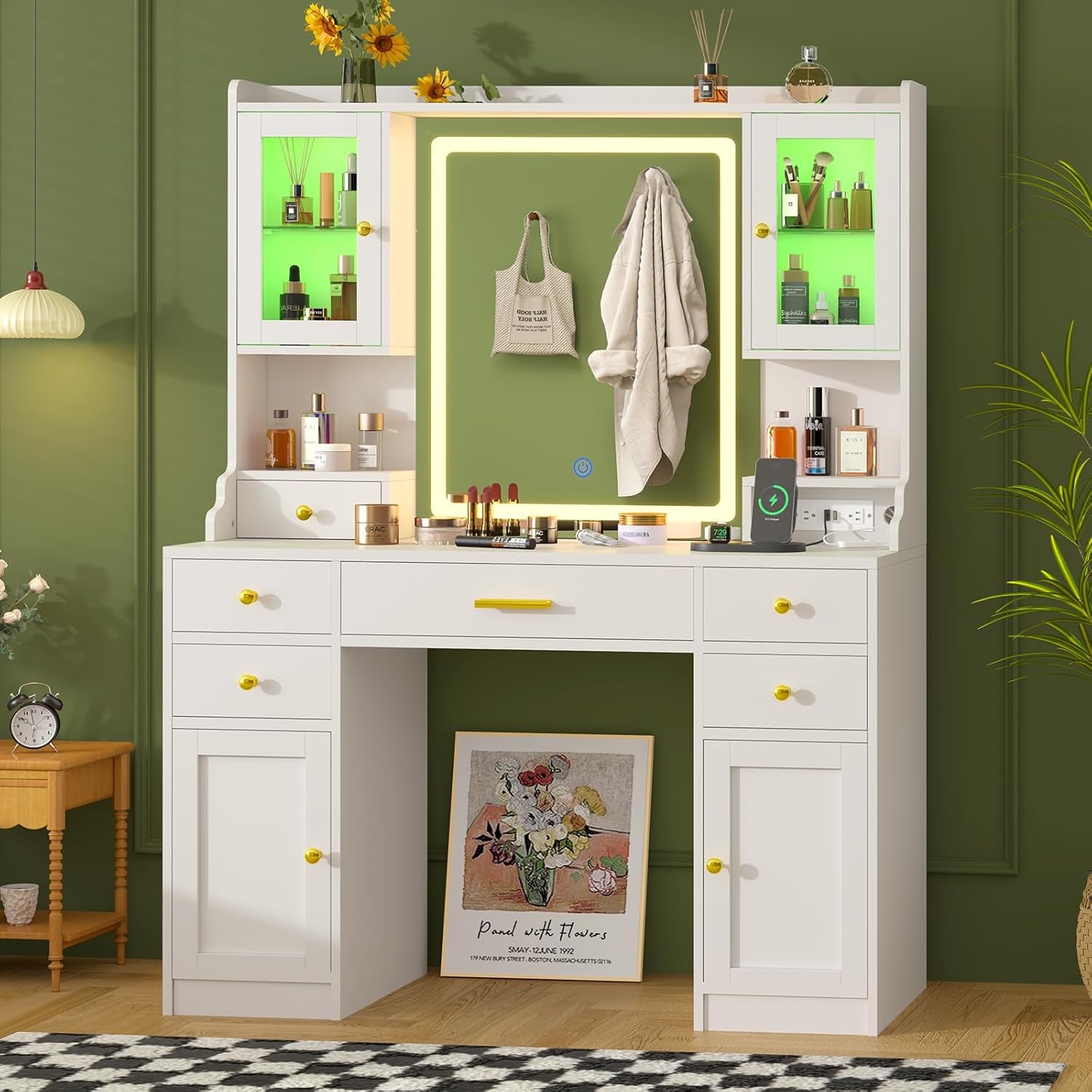 White vanity against a green wall with green-tinted cabinet lighting and a coat hanging on the mirror