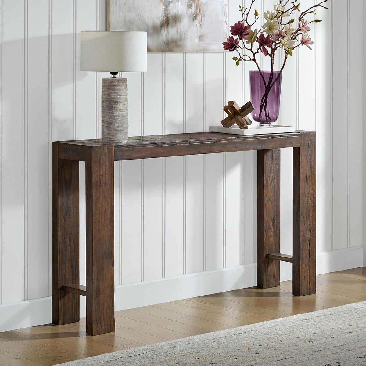Brown solid pine console table close-up with lamp and vase on the tabletop against a white paneled wall