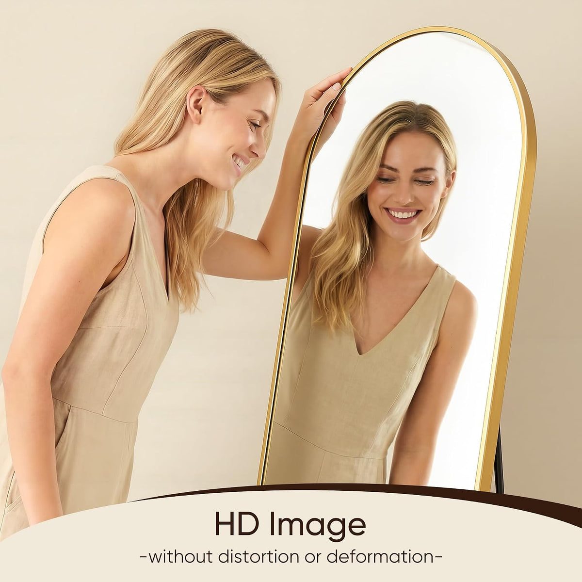 Woman smiling as she adjusts an arched gold full-length mirror that reflects her image.