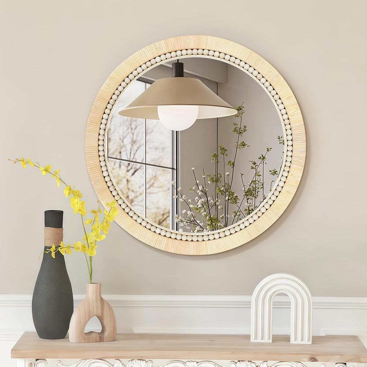 Hand‑woven rattan mirror with bead trim displayed over a console table reflecting a pendant light