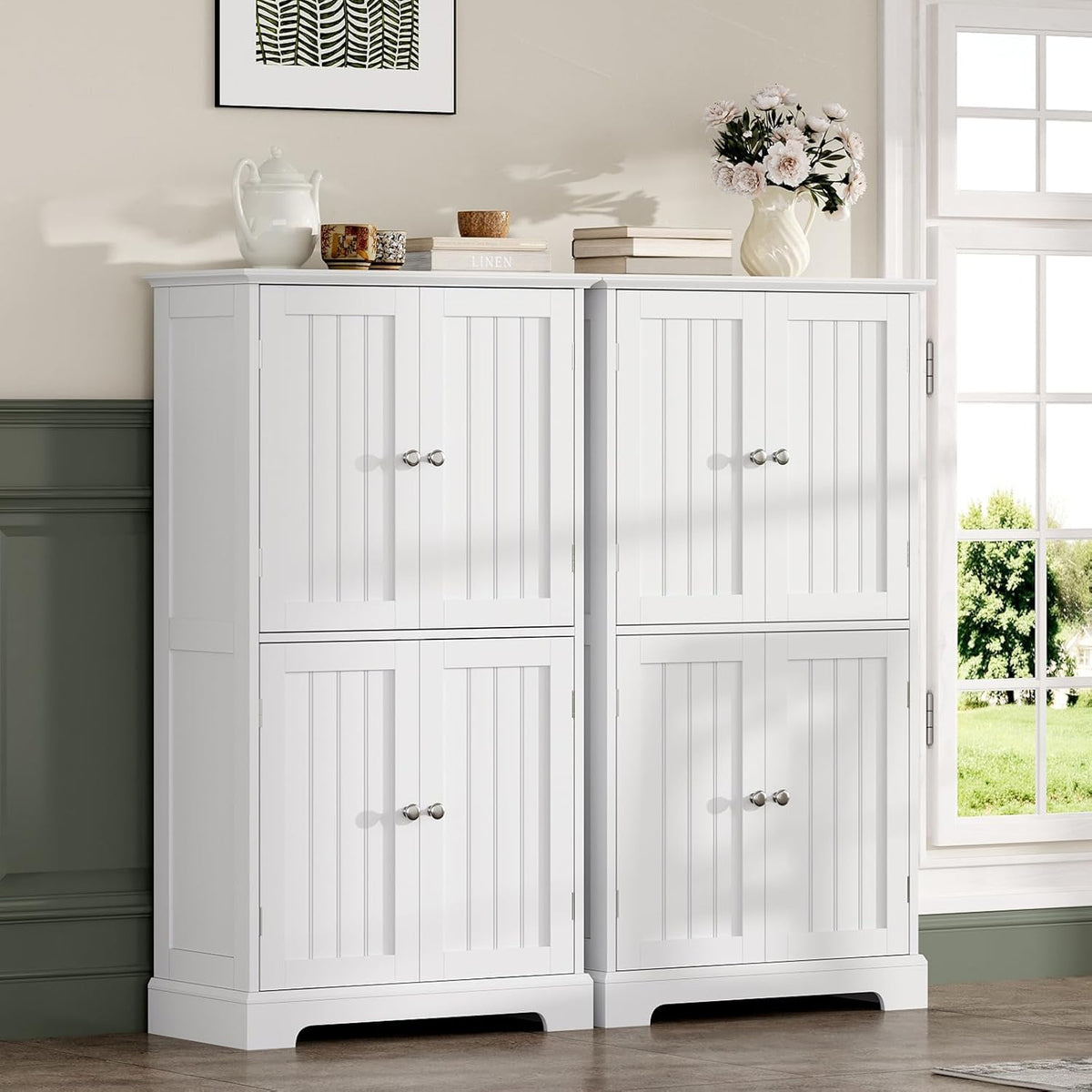 Two matching white floor cabinets placed side by side by a window, styled with vases and books on top.