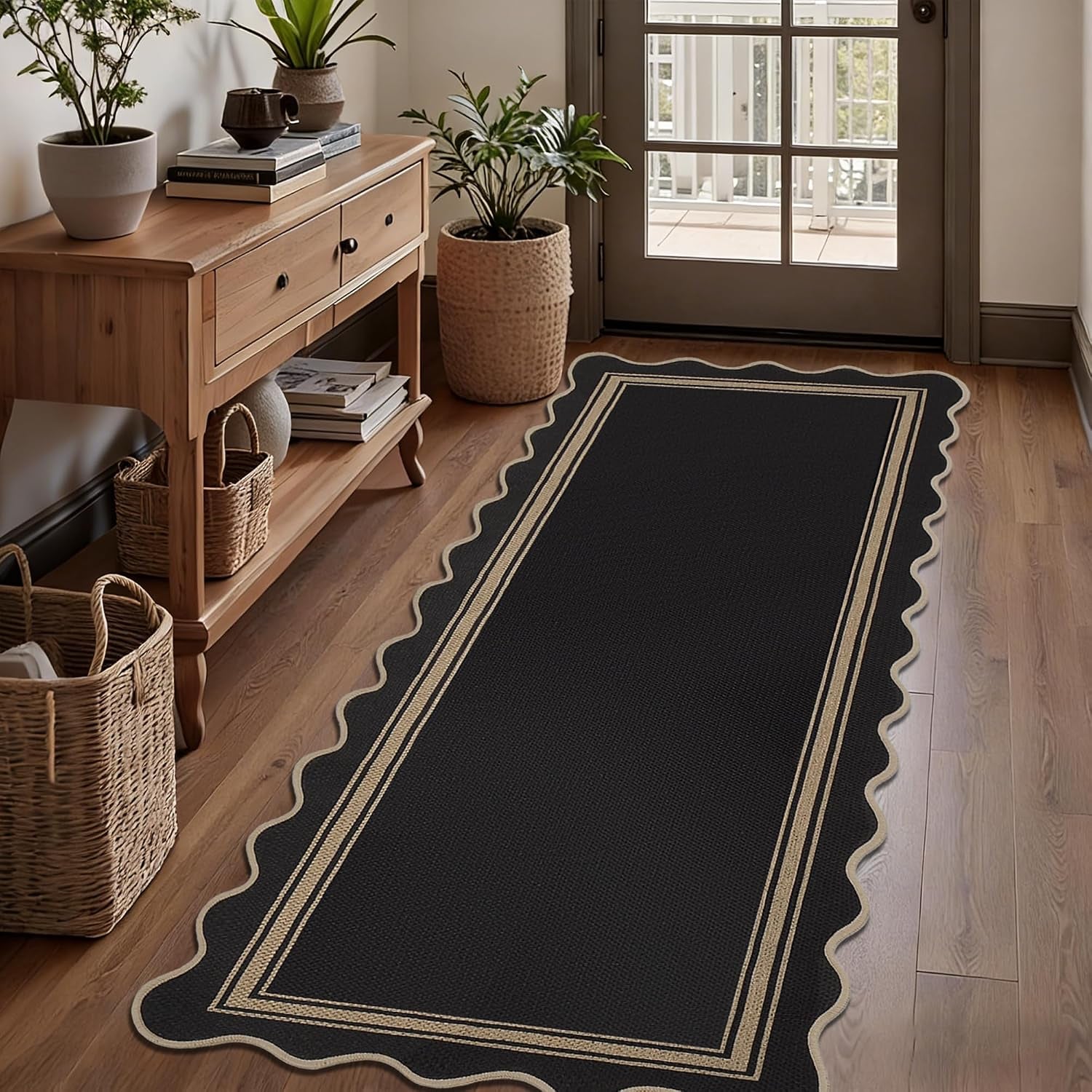 Hallway runner view of a scalloped black rug beside a wooden console and potted plant.