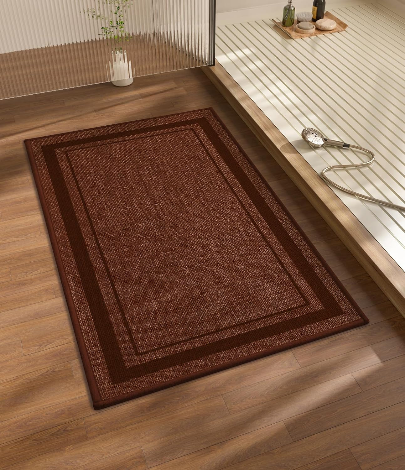 Rectangular dark brown bath rug with double border placed on wood floor beside a shower platform.