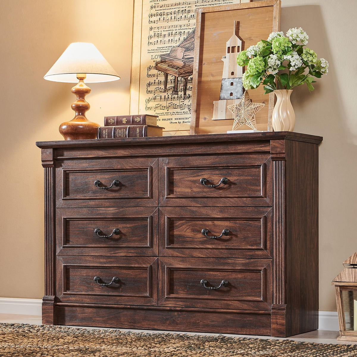 Front view of a dark brown wooden six-drawer dresser topped with a lamp, books, and framed art.