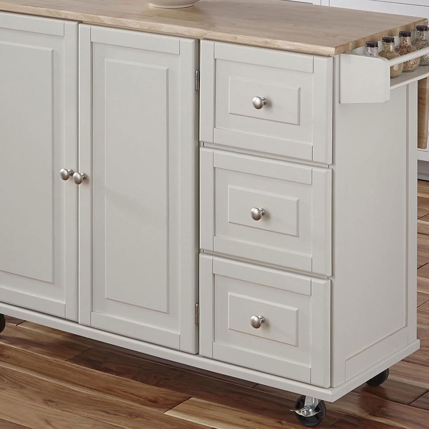 Close-up side view of off-white kitchen island drawers, cabinet door, wood top and caster on hardwood floor.