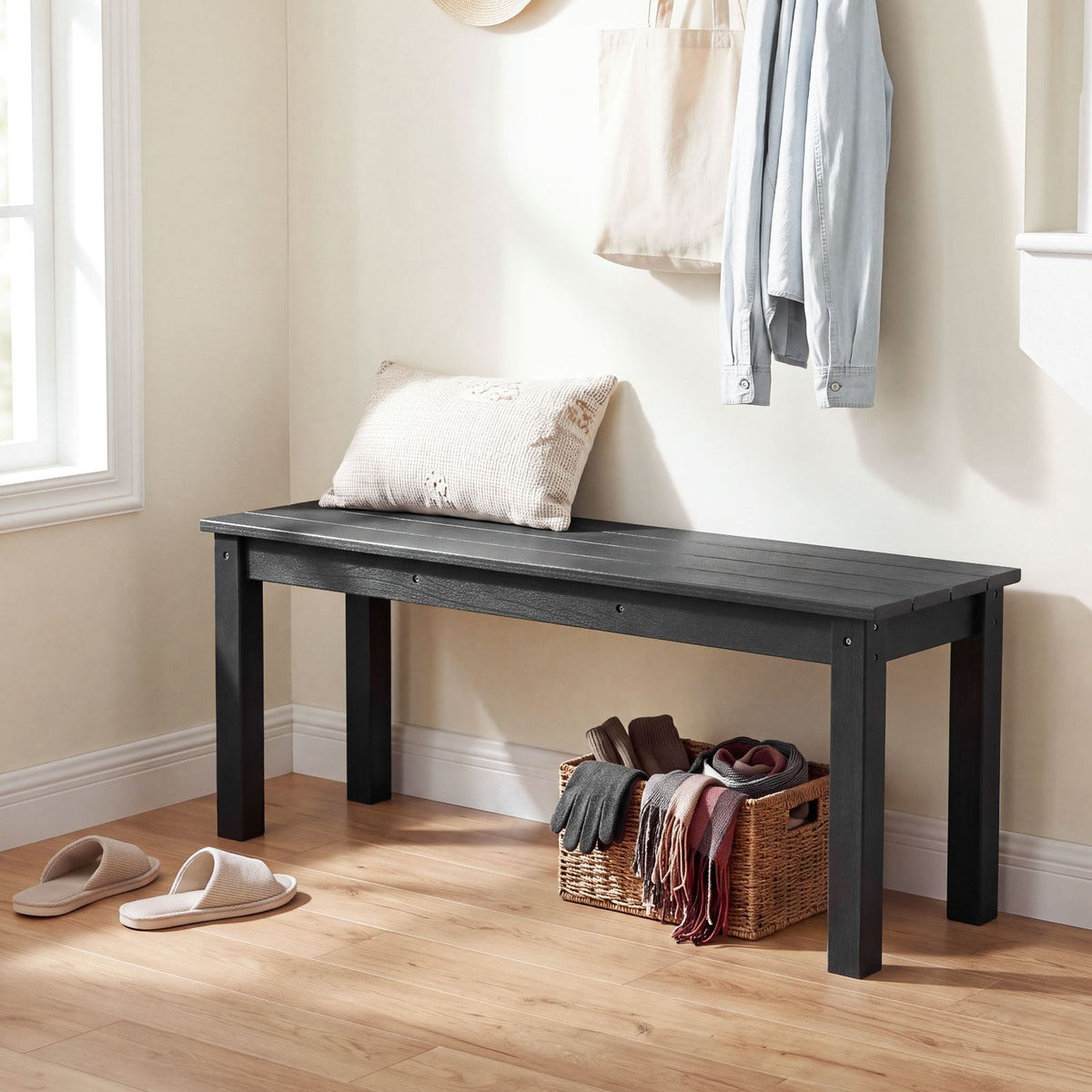 Black slatted bench styled in a bright entryway beside a basket and slippers.