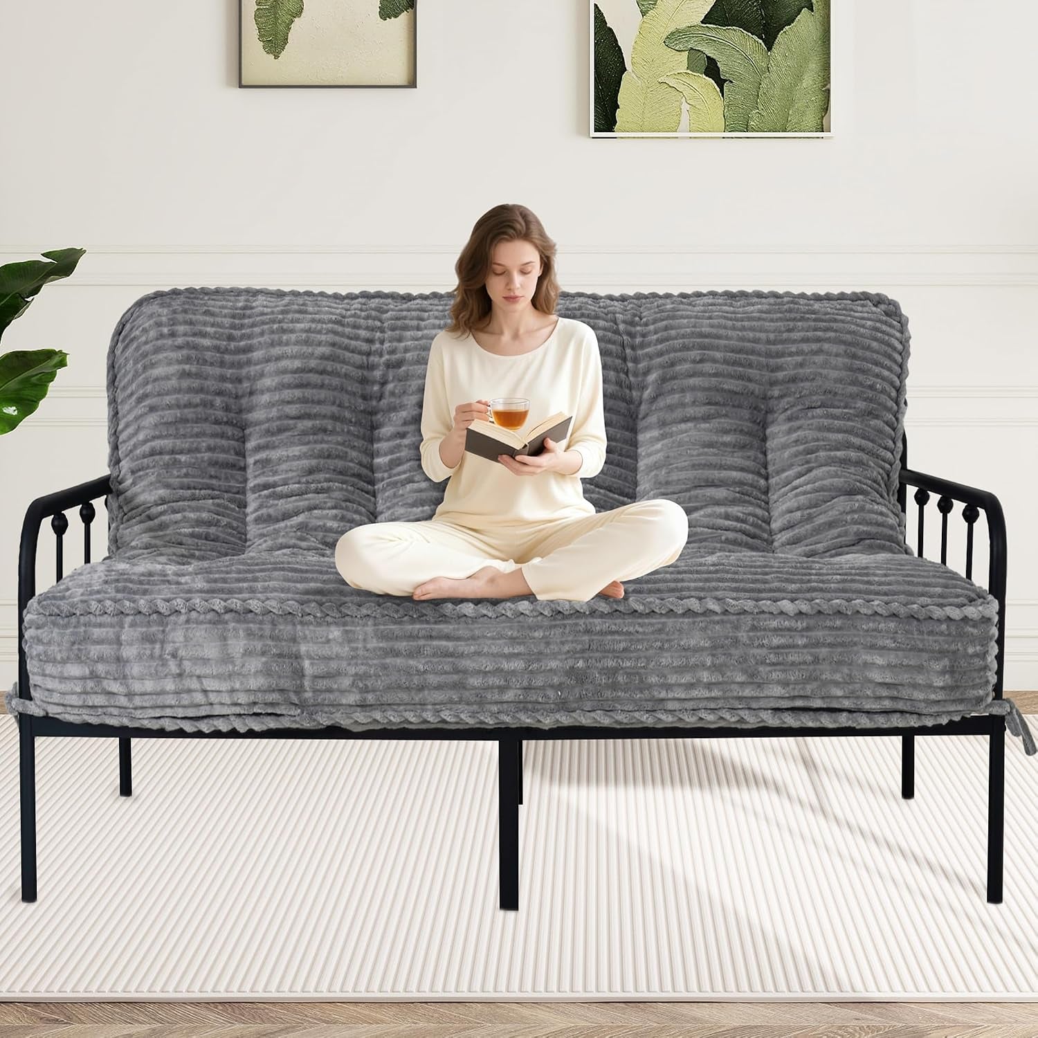 Woman sitting cross-legged on a ribbed dark gray futon mattress placed on a black metal frame
