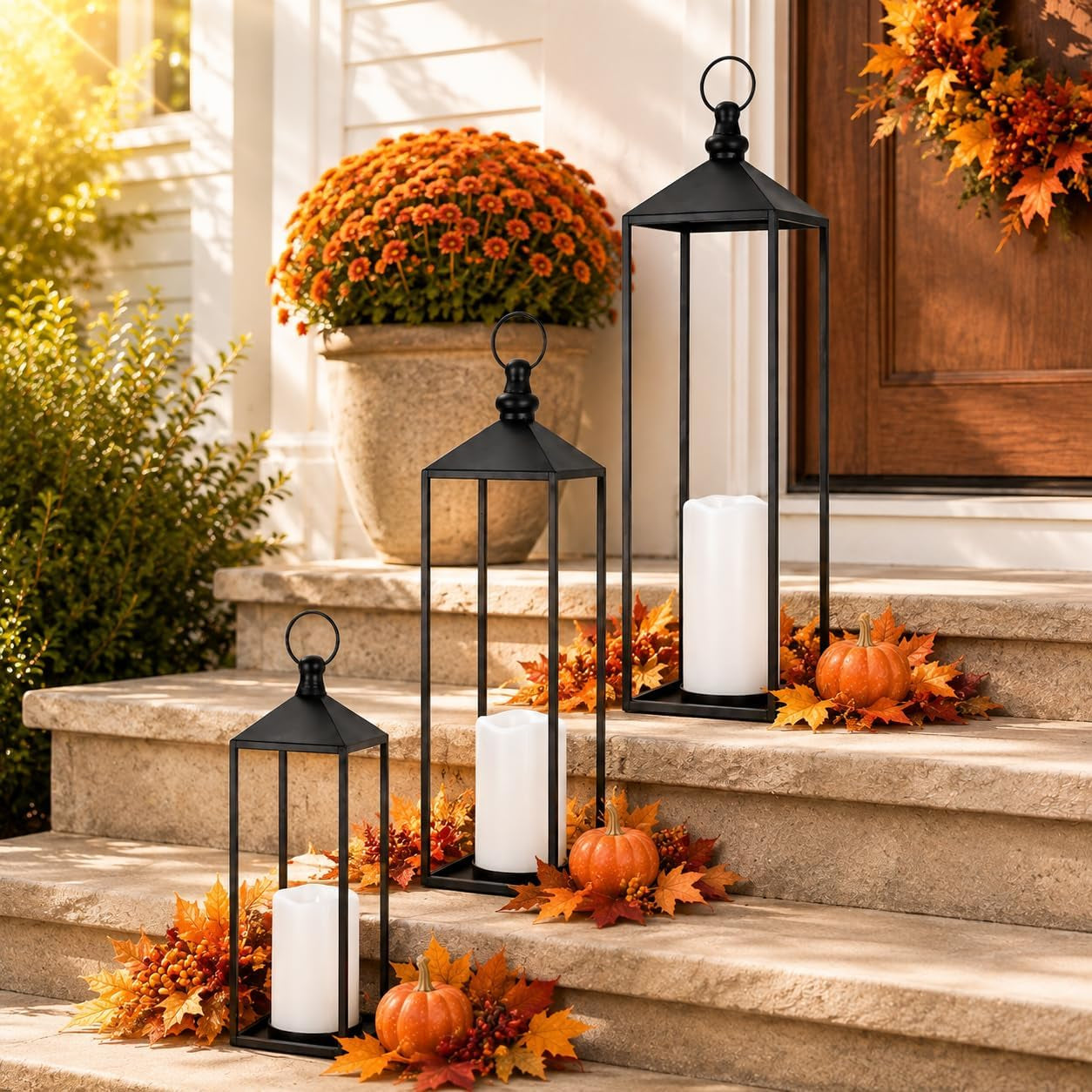 Three black lanterns with LED candles displayed on front steps with fall decor and small pumpkins