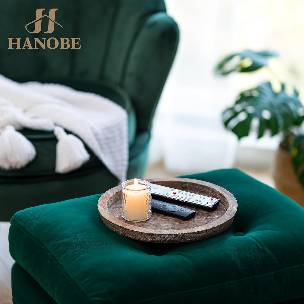 Round wooden tray on a green ottoman holding a lit candle and two remote controls.