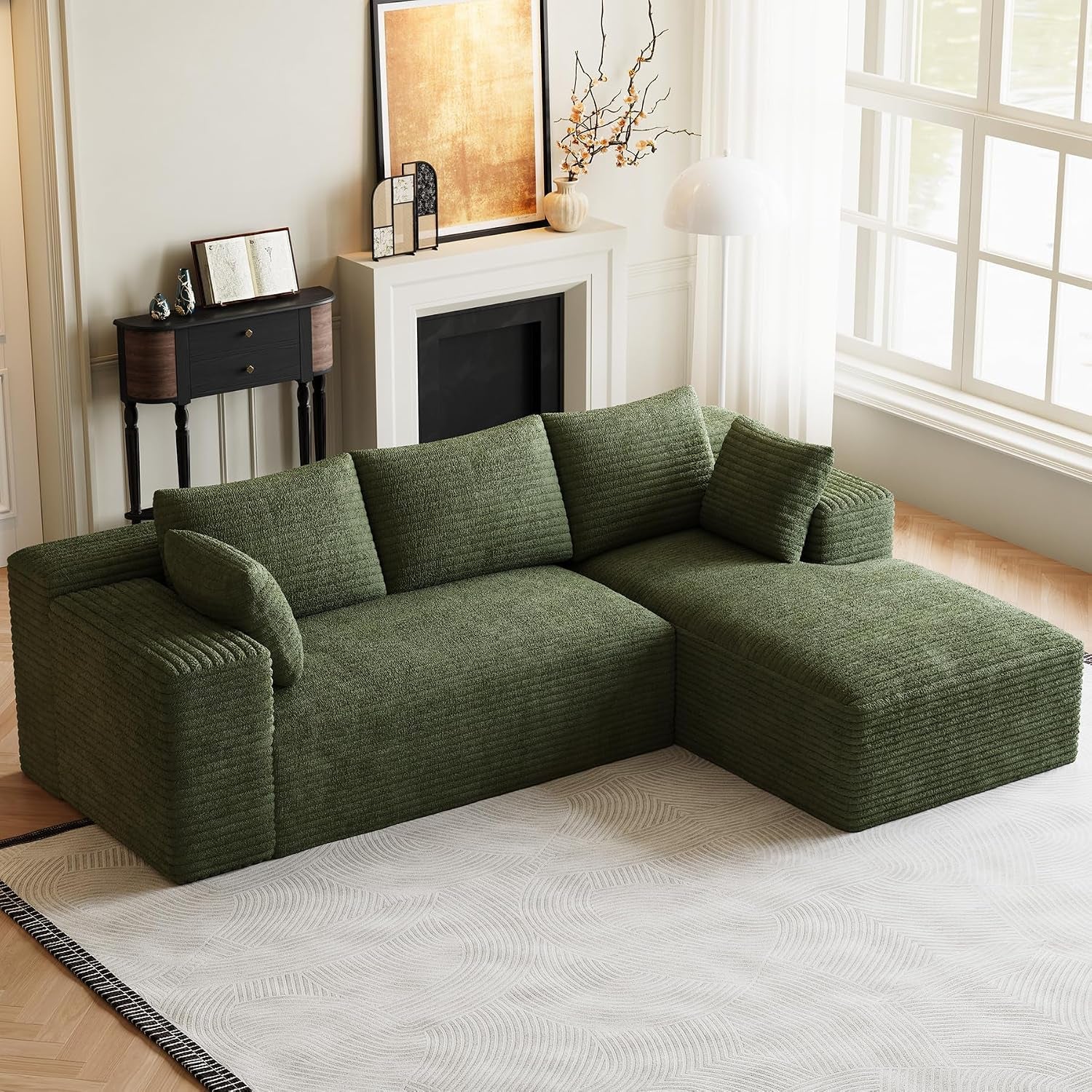 Green L-shaped sectional with chaise and matching pillows positioned by a window and fireplace.