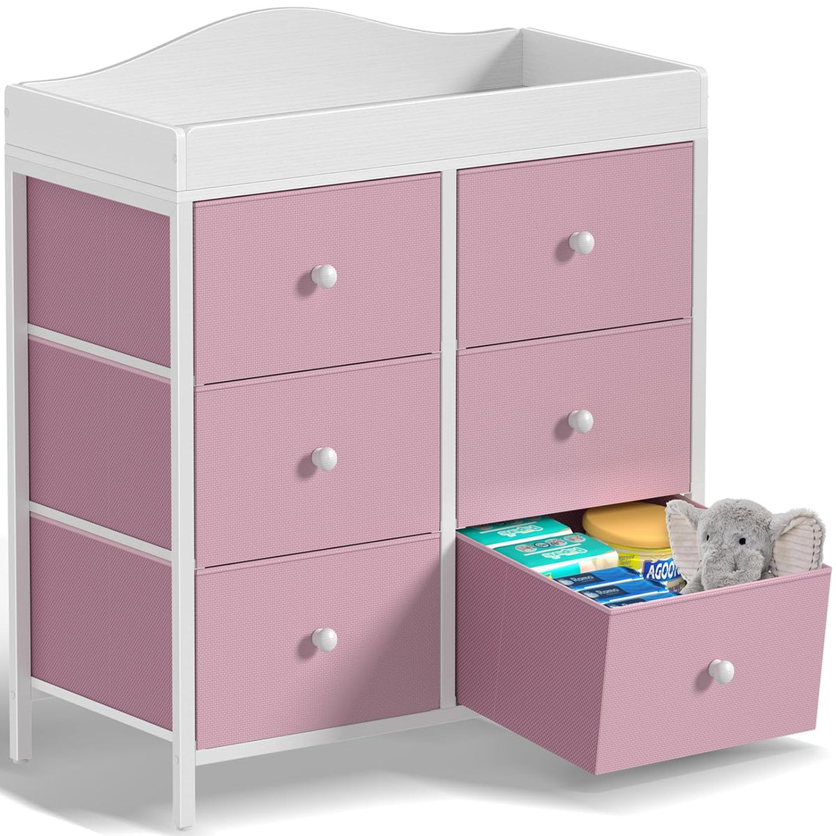 White-framed changing dresser with pink drawer fronts, one drawer open holding baby items and a stuffed elephant.