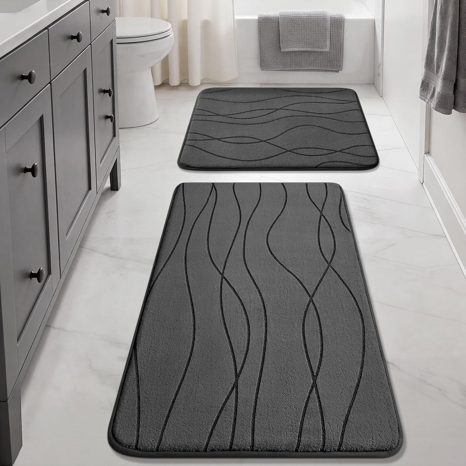 Two dark-gray wavy-pattern mats aligned down the bathroom floor between a gray vanity and a tub