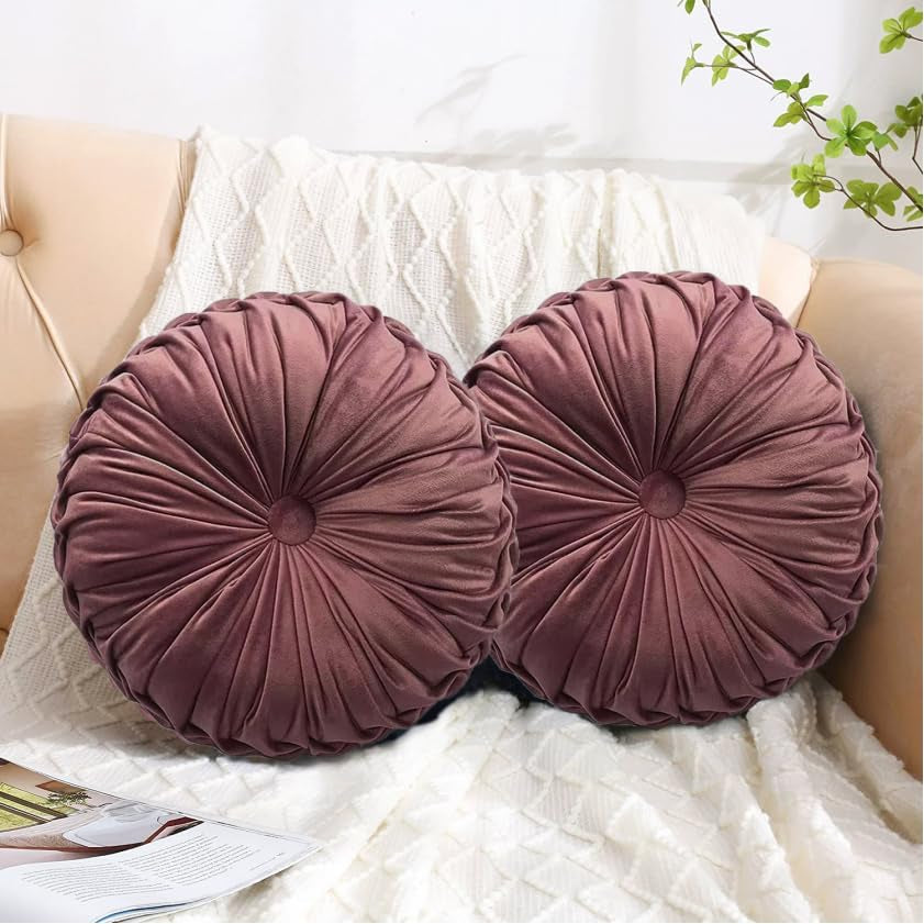 Two mauve round ruched pillows propped on a cream knit blanket over a beige sofa.