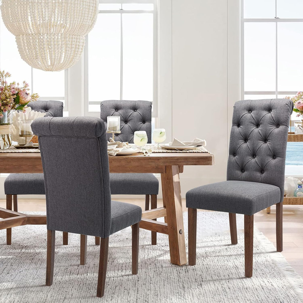 Dining room scene with dark gray tufted chairs around a wooden trestle table and a beaded chandelier